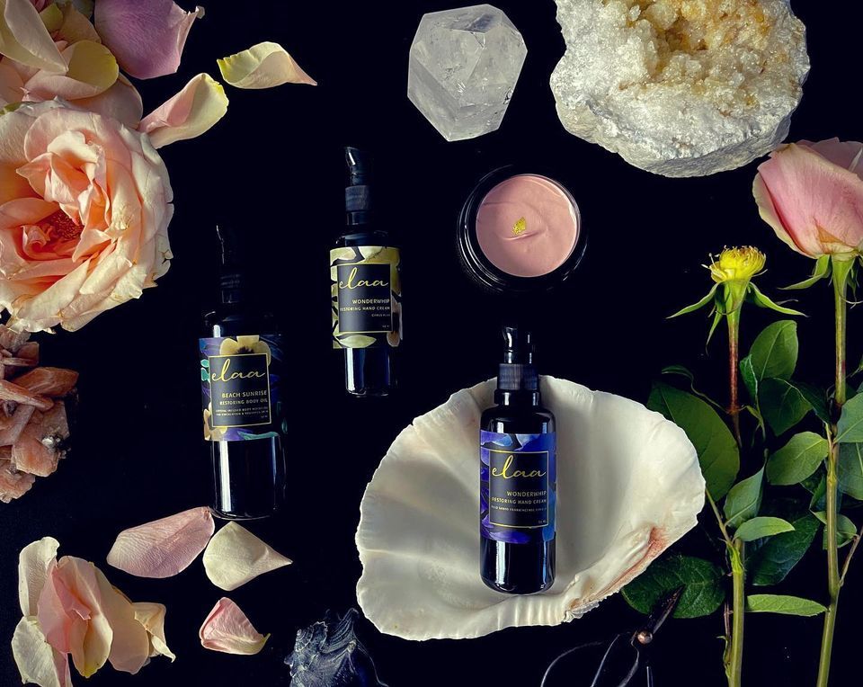 Botanical skincare display with dark bottles, pink roses, white shell, crystals, and a pink candle on black background