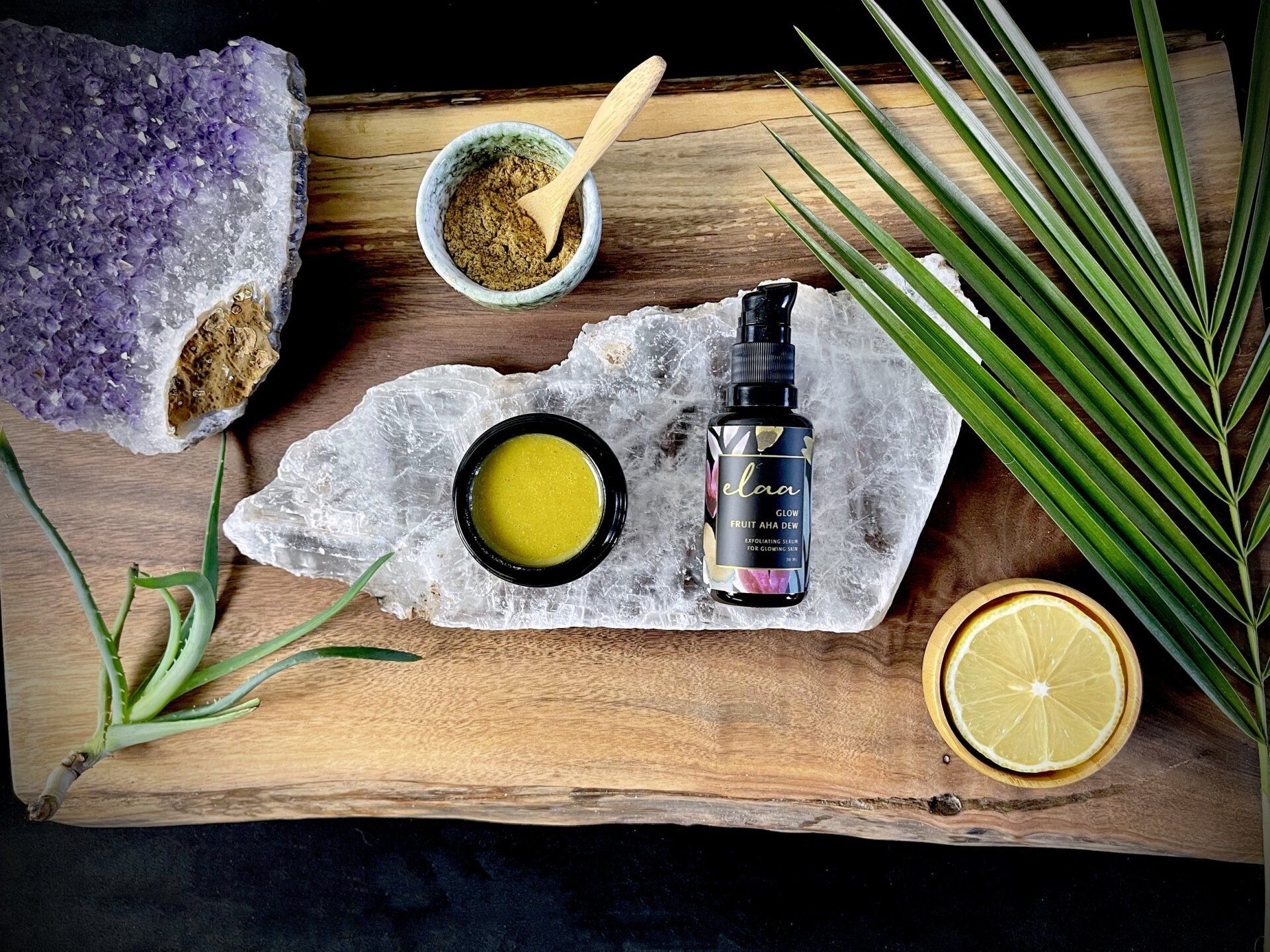 Flat lay of natural skincare items on a wooden surface with stones, leaves, a lemon slice, and essential oil bottle