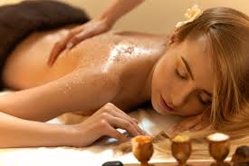 Person receiving a back massage on a spa table, with oil and candles nearby.