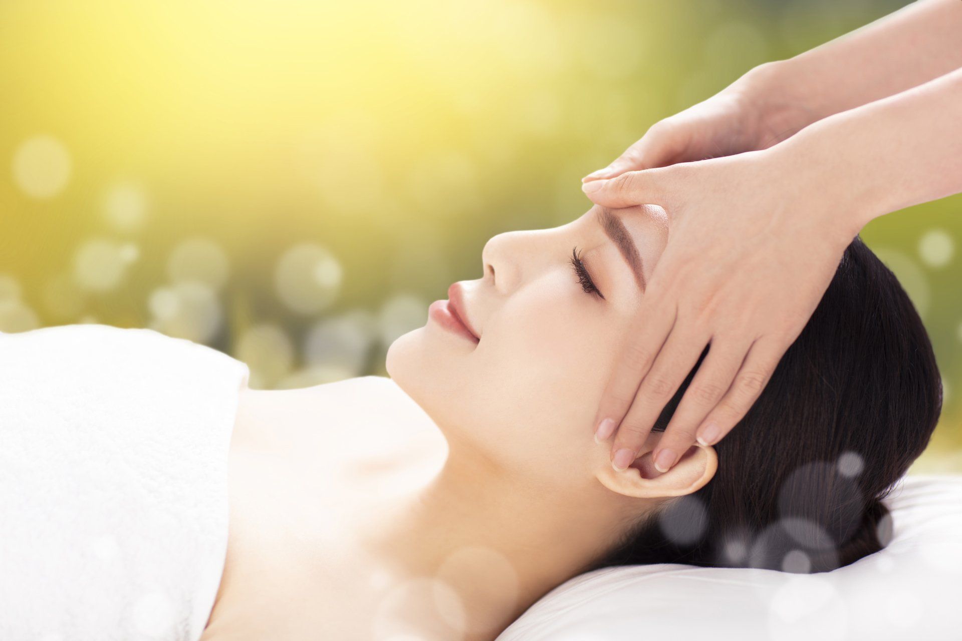 Person receiving a facial massage with hands on temples in a bright spa setting