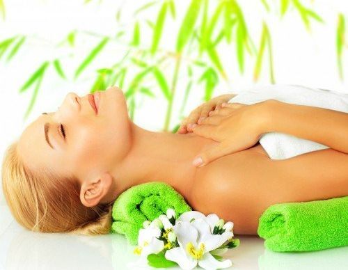 Person lying on a spa table with green towels and white flowers, in a relaxing massage setting