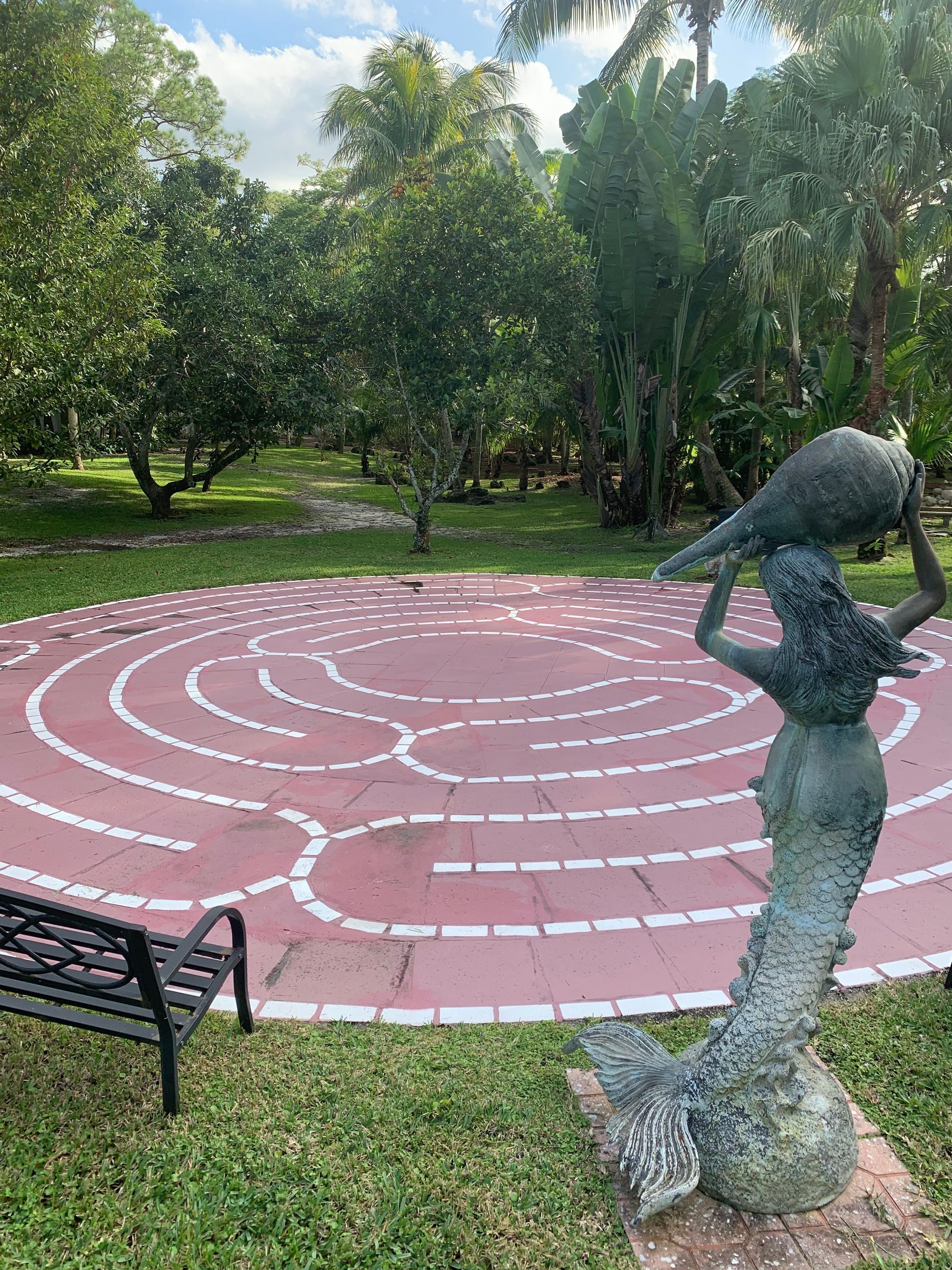 Garden labyrinth with a bench and a bird sculpture in a grassy park