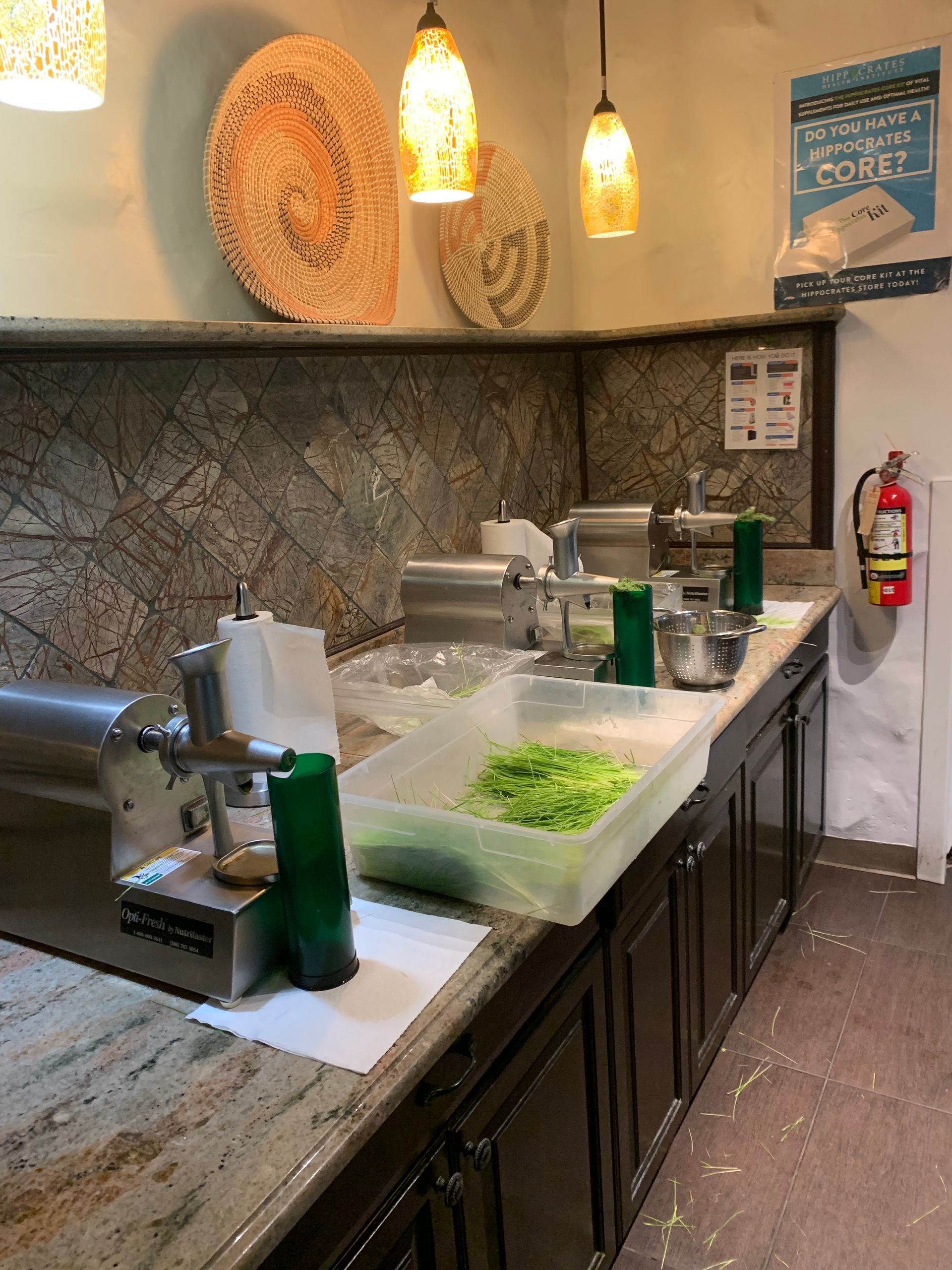 Restaurant kitchen prep counter with lettuce bins, utensils, and stone backsplash under warm pendant lights