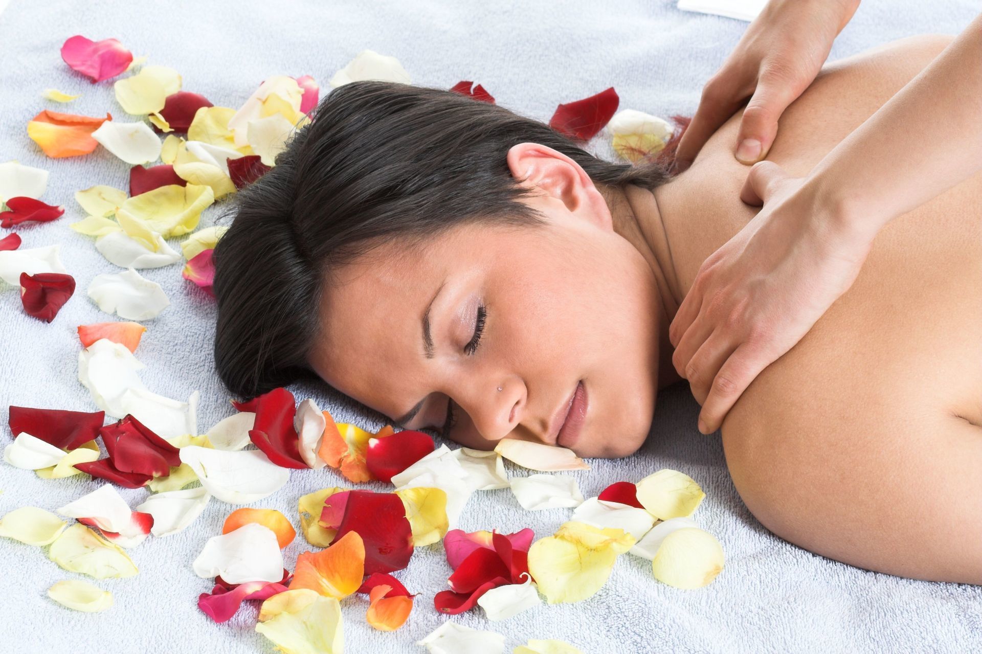 Woman receiving a shoulder massage with flower petals around her face on a white towel