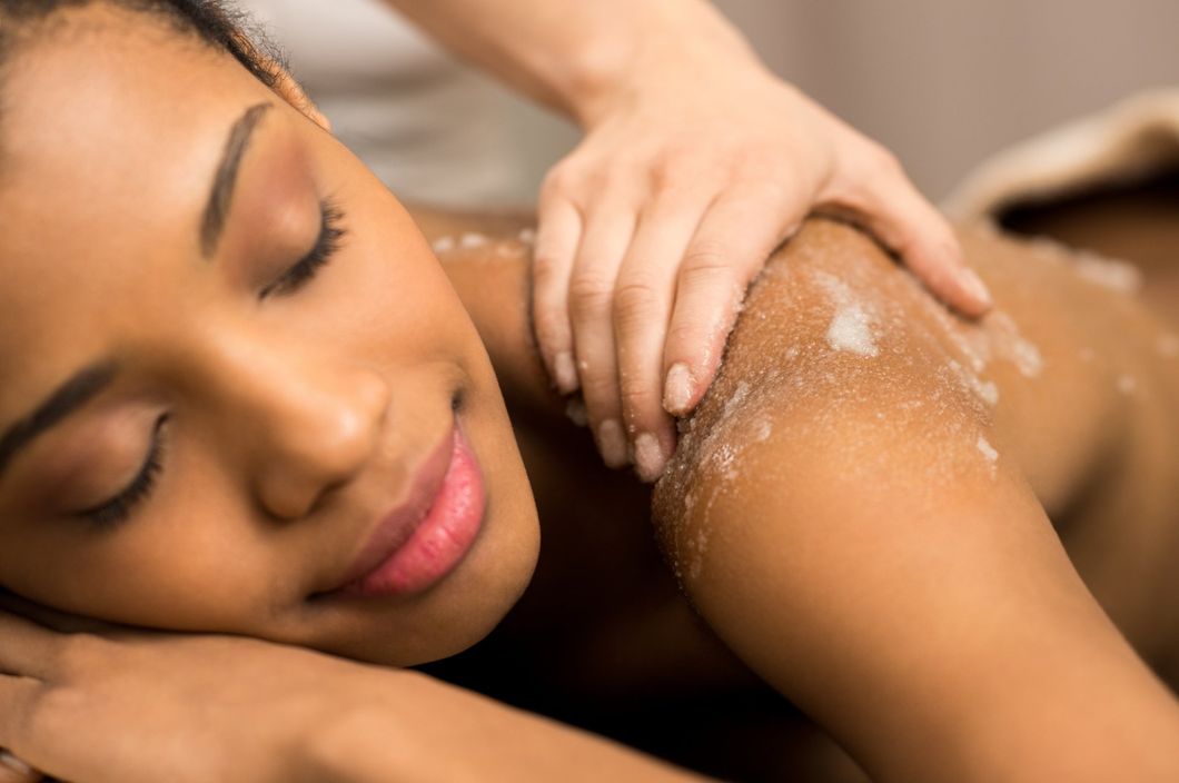 Person receiving a shoulder massage with exfoliating scrub on the skin, eyes closed and relaxed