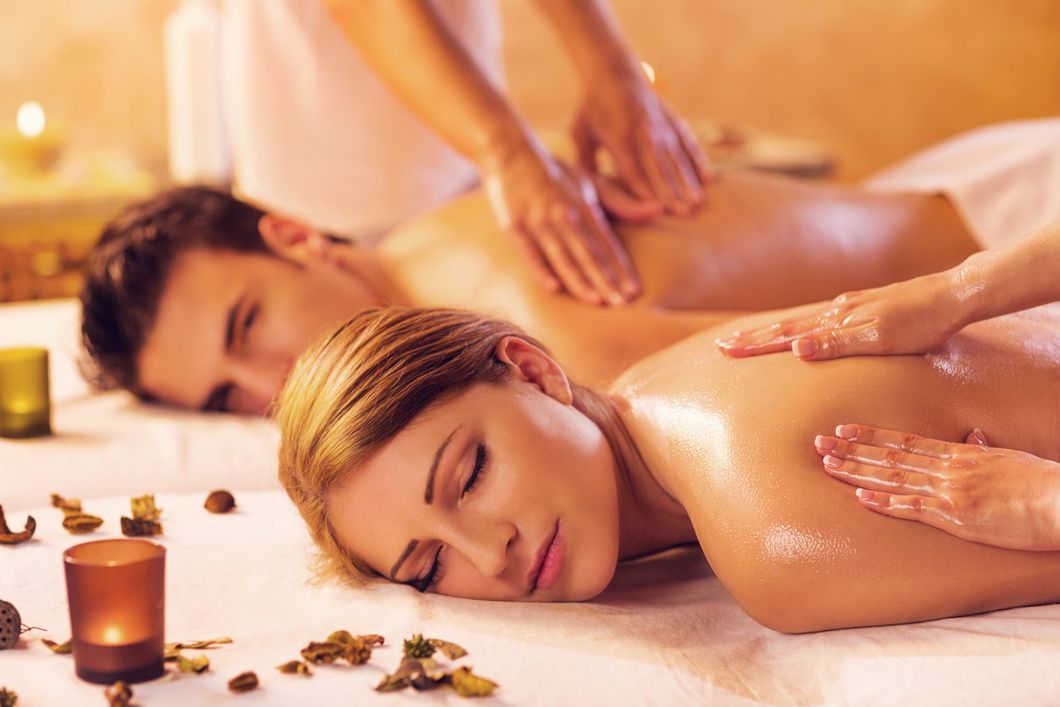 Relaxing spa massage with two clients lying face down, warm candlelight, and soothing oil applied on their backs