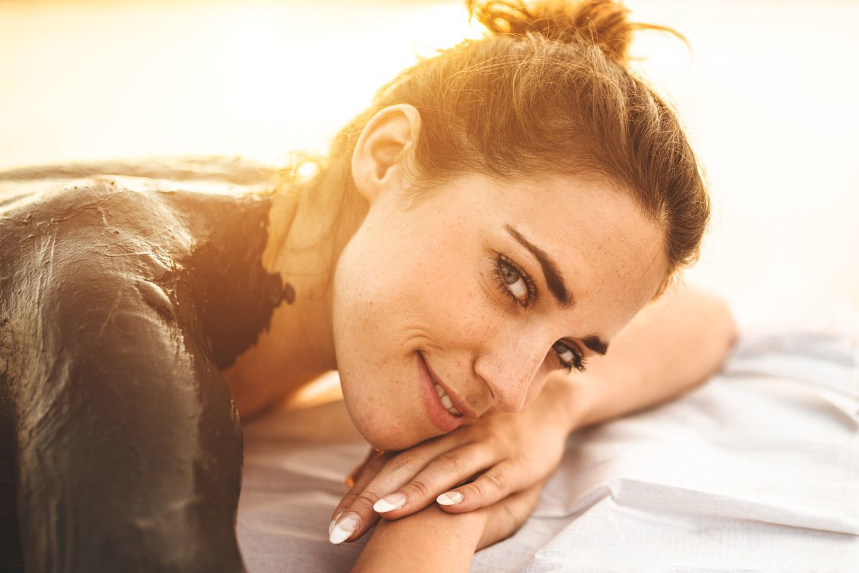 Woman lying on a bed, smiling softly in warm sunlight, resting her head on her hands.