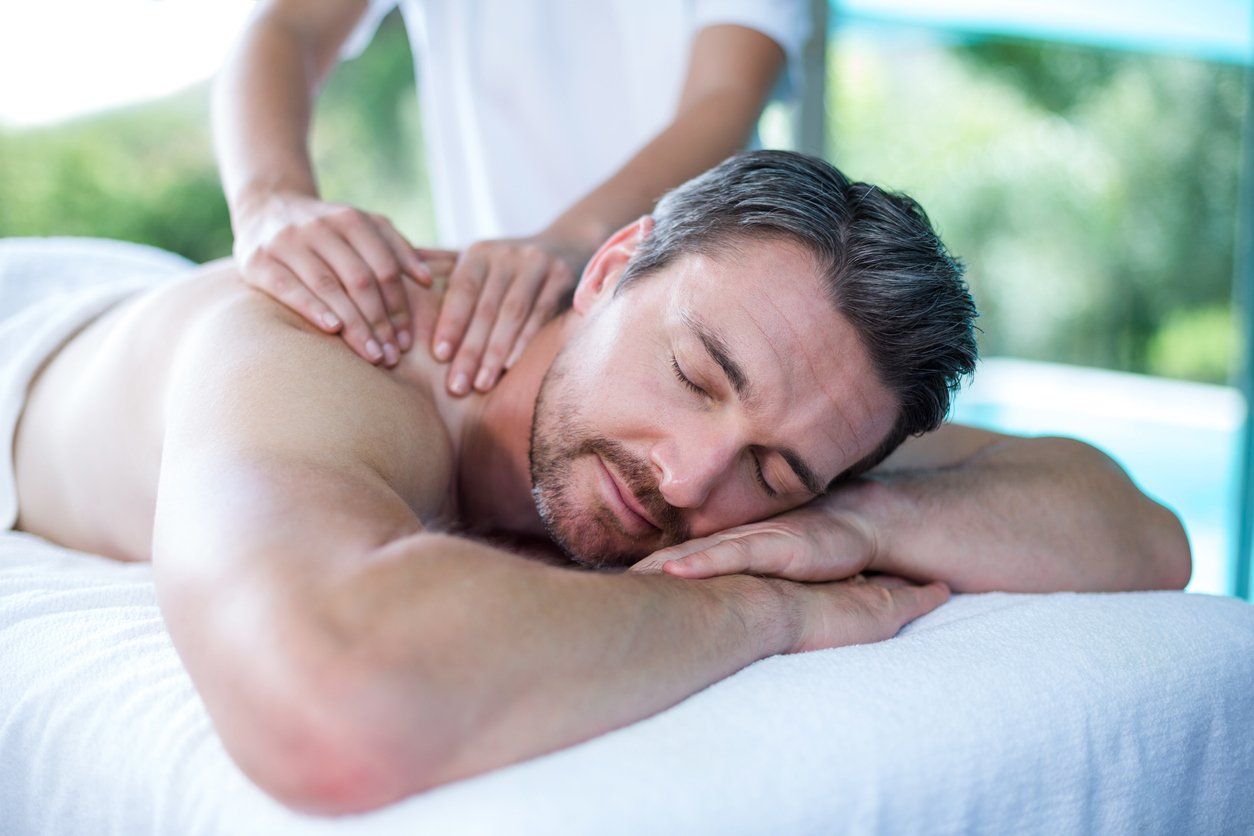 Person receiving a shoulder massage while lying on a table with eyes closed in a spa setting