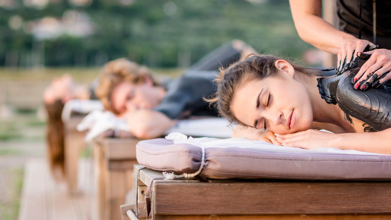 People lying face down on massage tables outdoors, receiving back massages in a spa setting