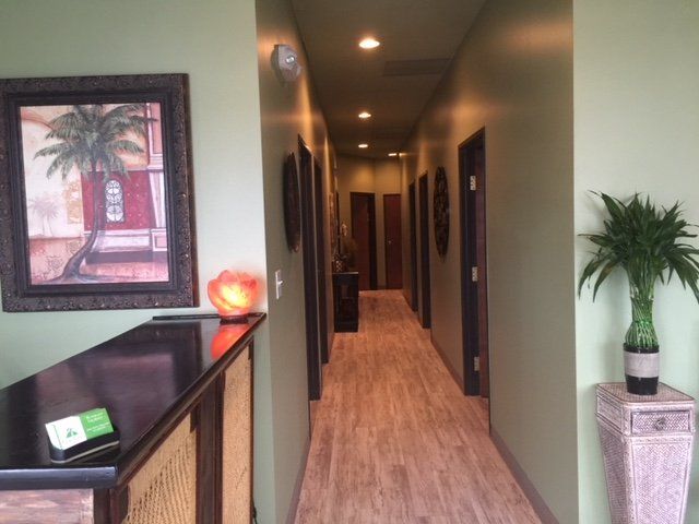 A narrow hallway with green walls, wood-look flooring, framed art, and potted plants.