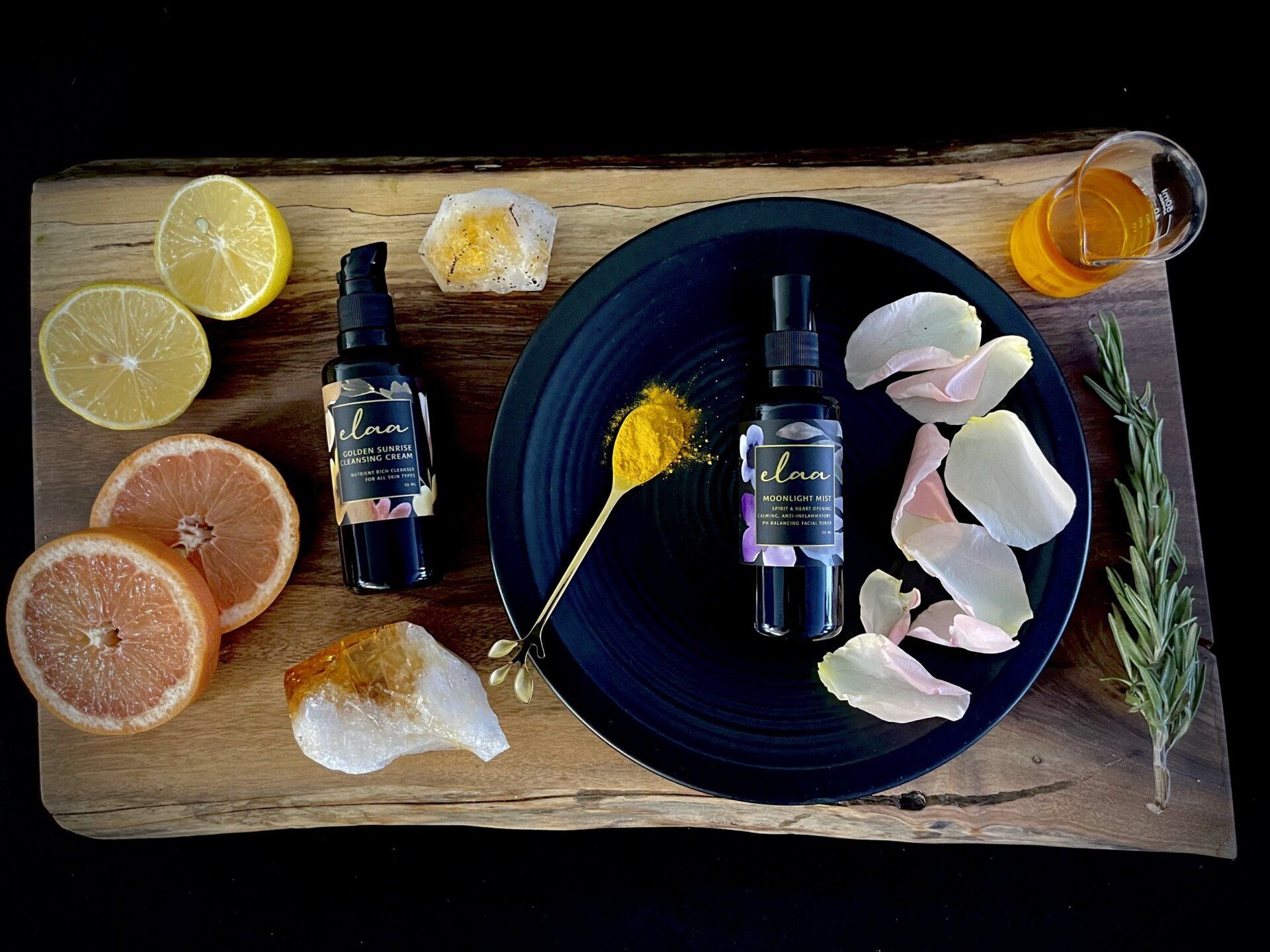 Aromatic spa still life with citrus slices, essential oil bottles, bath salts, flowers, and a rosemary sprig on wood.