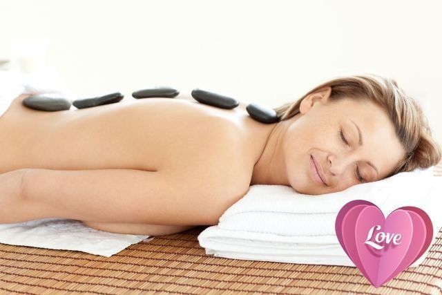 Woman lying face down on massage table with hot stones on her back, resting on white pillow with pink heart
