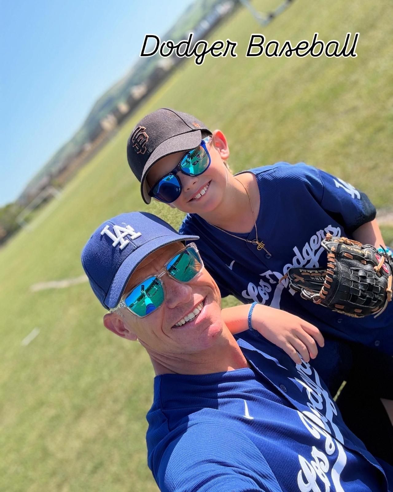 Man and boy in Dodger baseball gear smiling, outdoors on a sunny day.