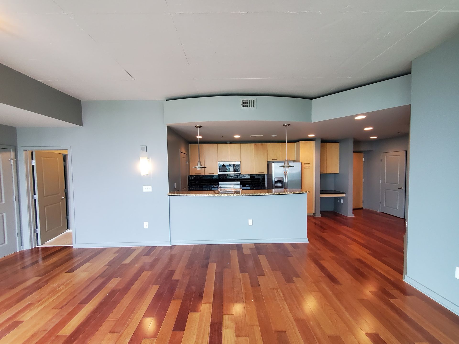 Interior of a condo: hardwood floors, open kitchen with stainless steel appliances, light gray walls.