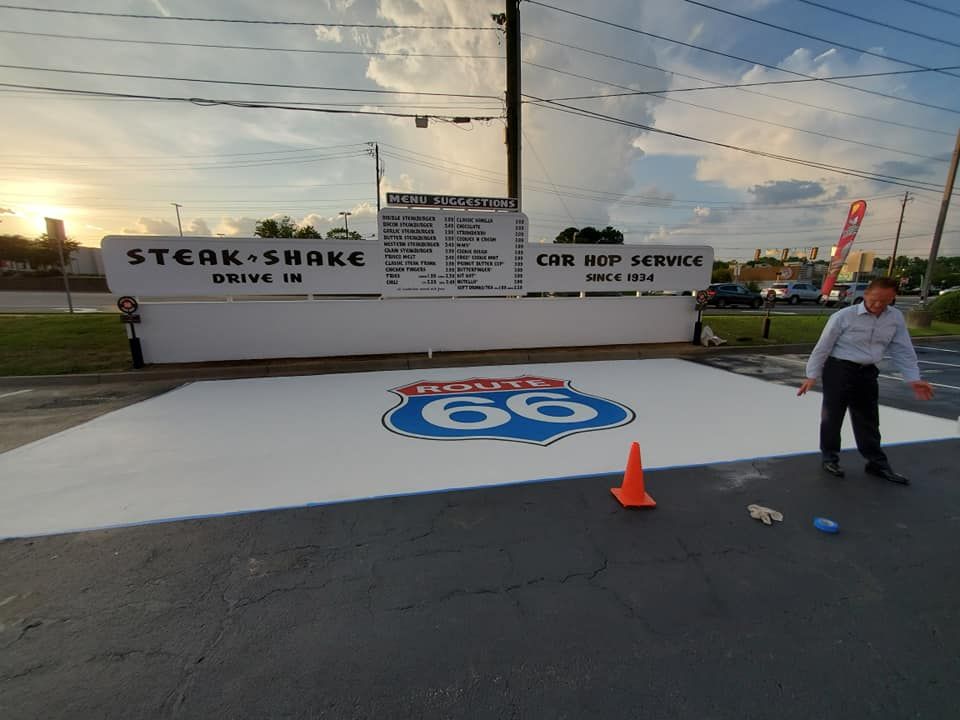 Man by a Steak 'n Shake with a Route 66 logo on the ground. A menu is displayed; drive-in setting.
