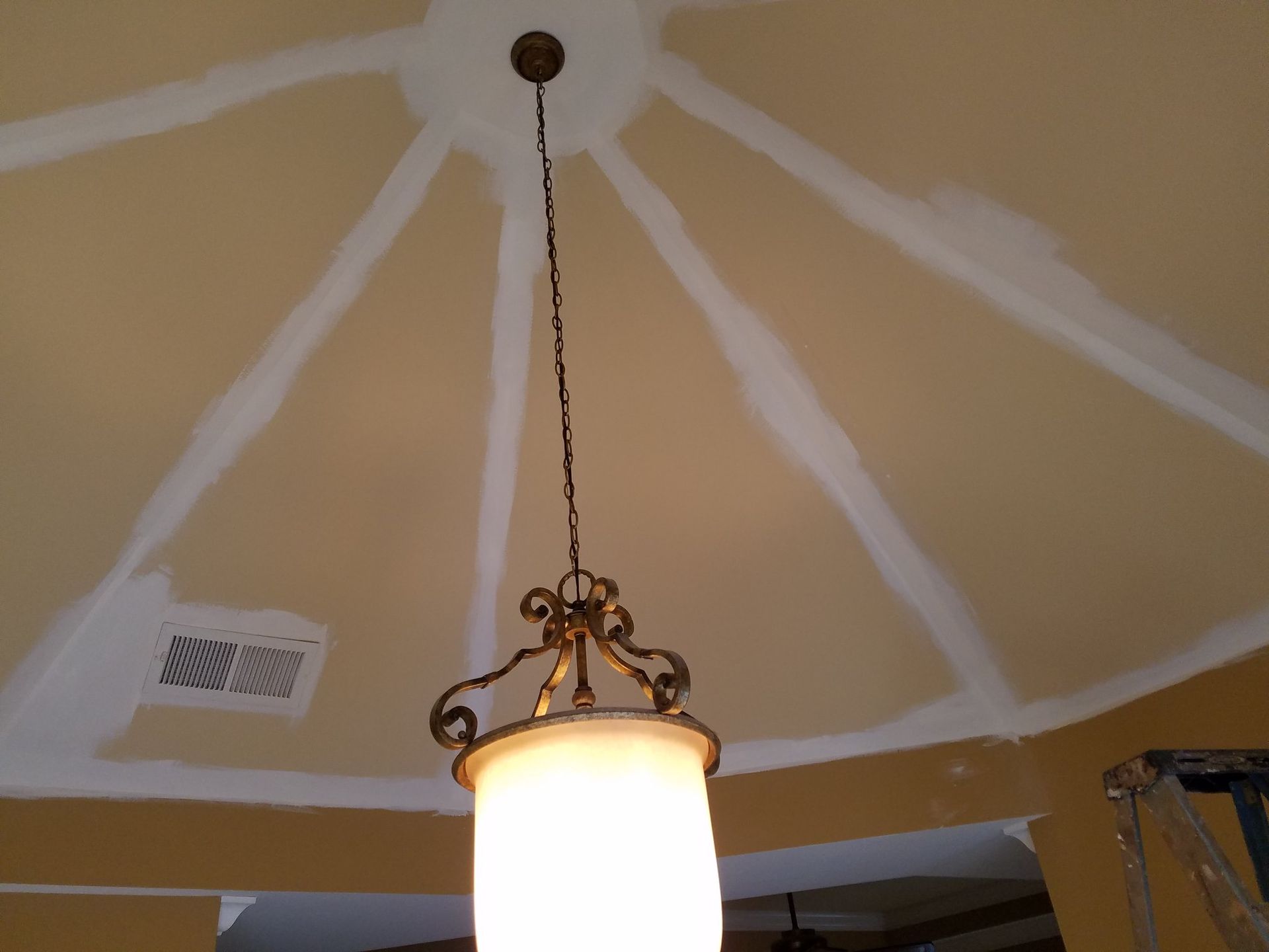 Beige ceiling with white lines radiating from a central light fixture. A lit chandelier hangs below.