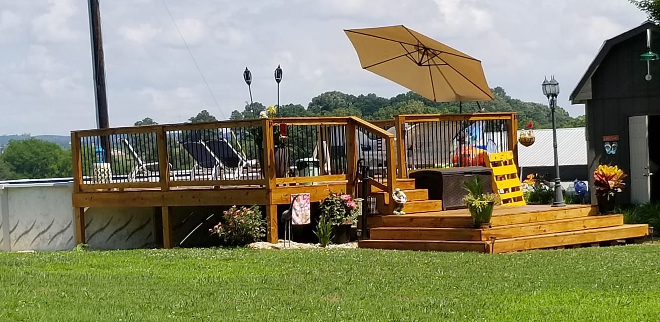 Wooden deck with pool, umbrella, and grassy yard. Barn in the background.