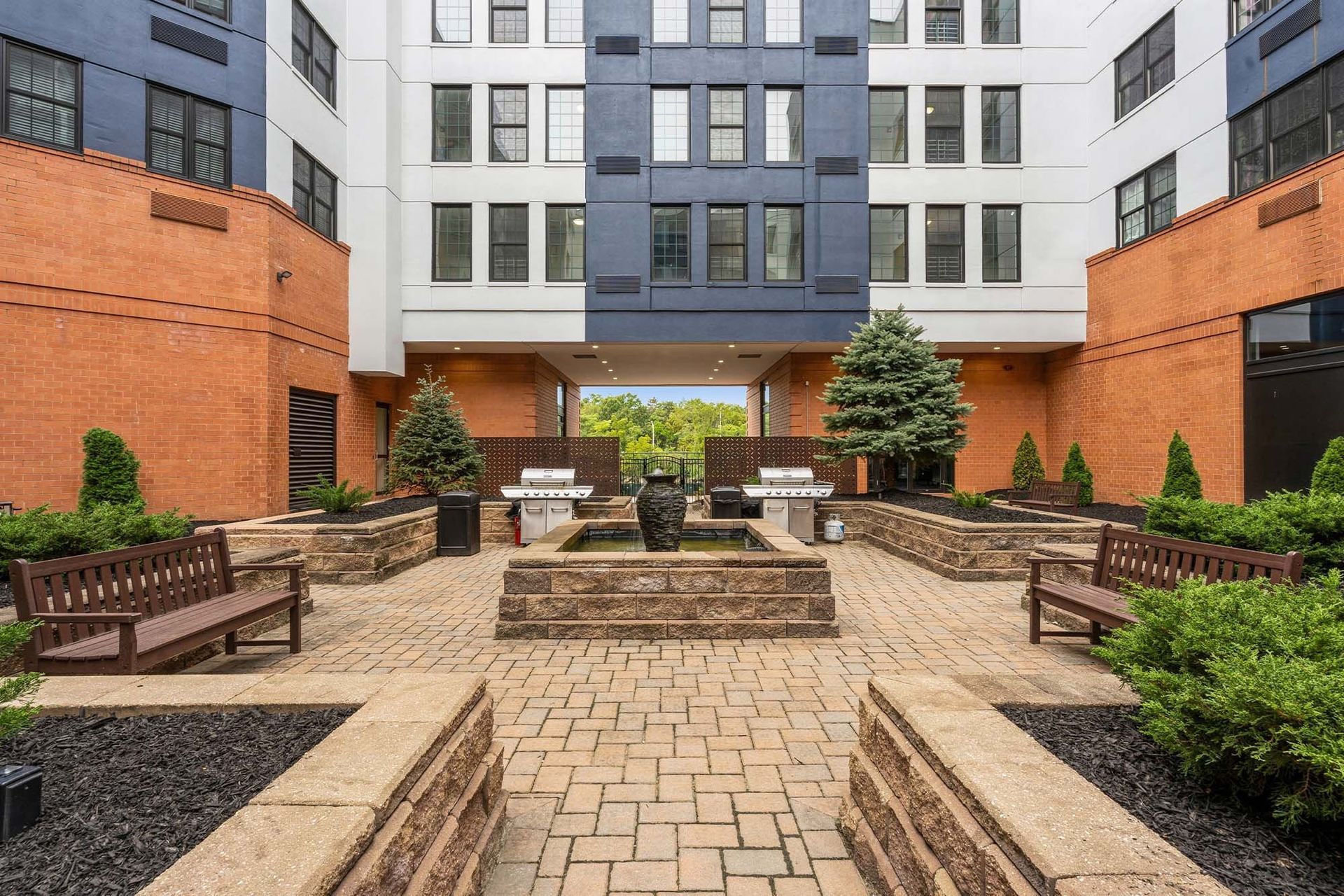 Outdoor communal courtyard with brick planters, benches, grills, and a central fountain Parc at Lyndhurst in Lyndhurst, NJ.