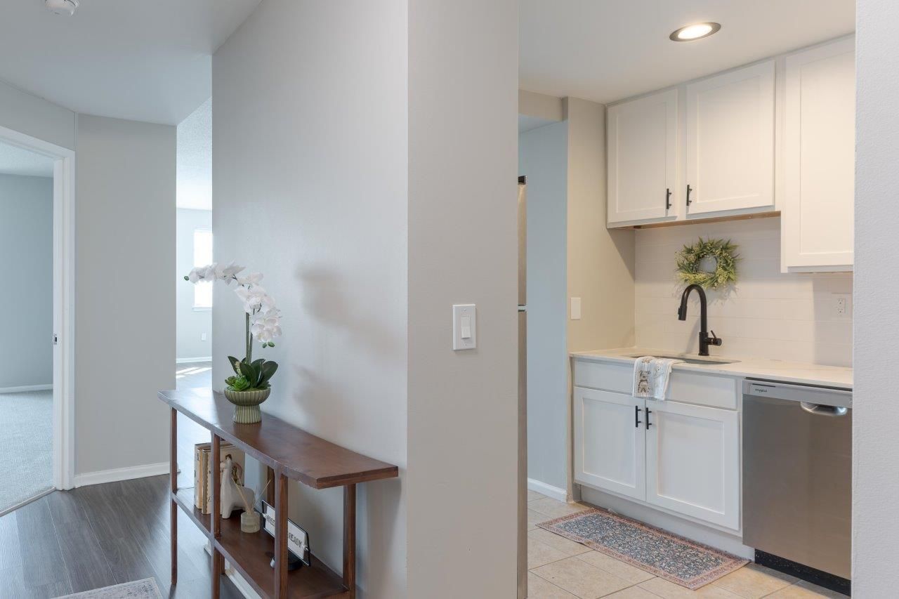 Bright hallway with a narrow table and orchid, opening to a small white kitchen with stainless dishwasher.