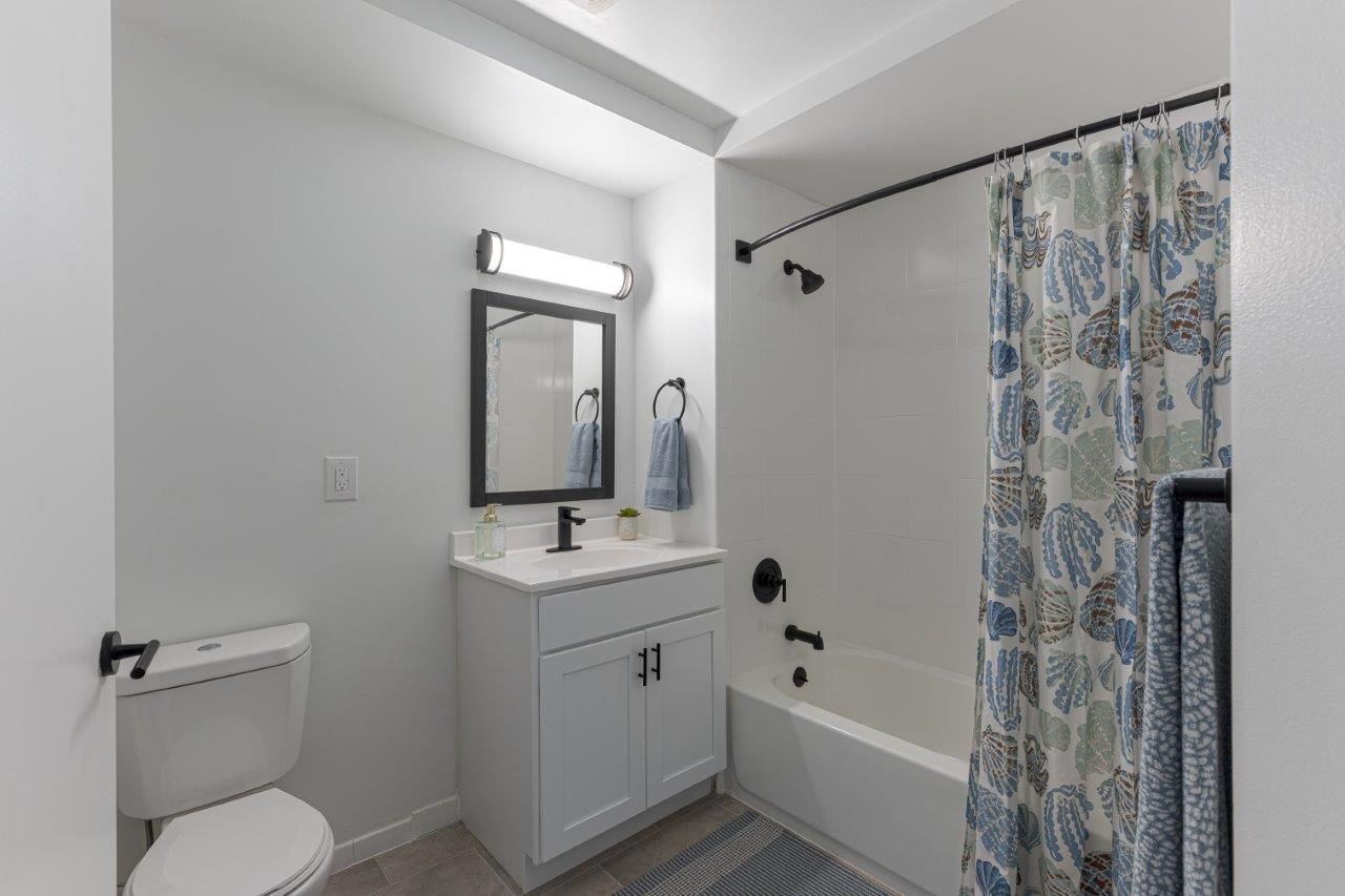 white bathroom with vanity, mirror light, toilet, and patterned shower curtain