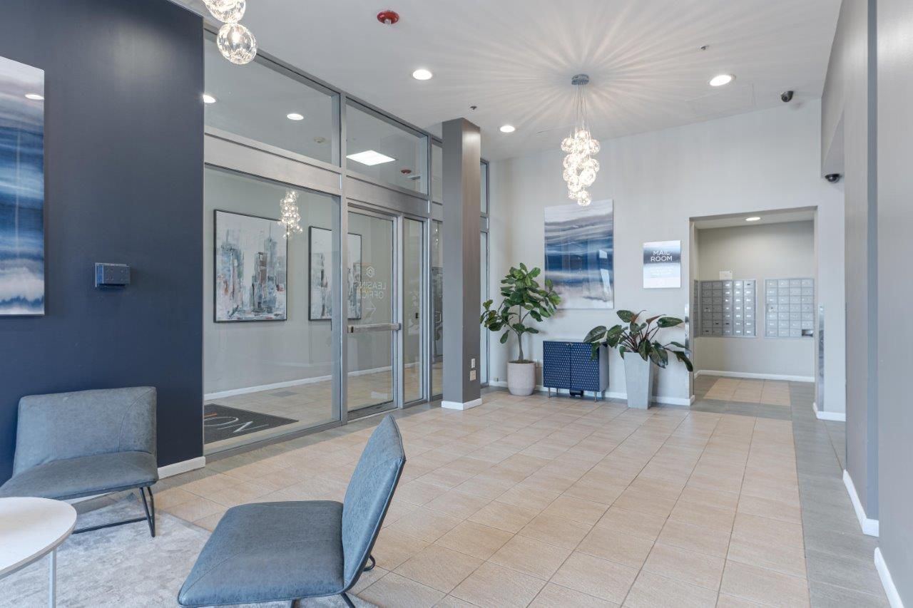 Modern lobby with glass doors, blue chairs, white walls, and potted plants