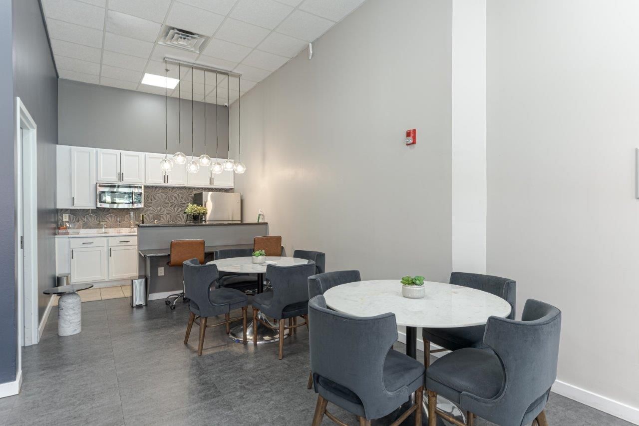 Resident lounge with round tables, gray chairs, a kitchenette, and white walls