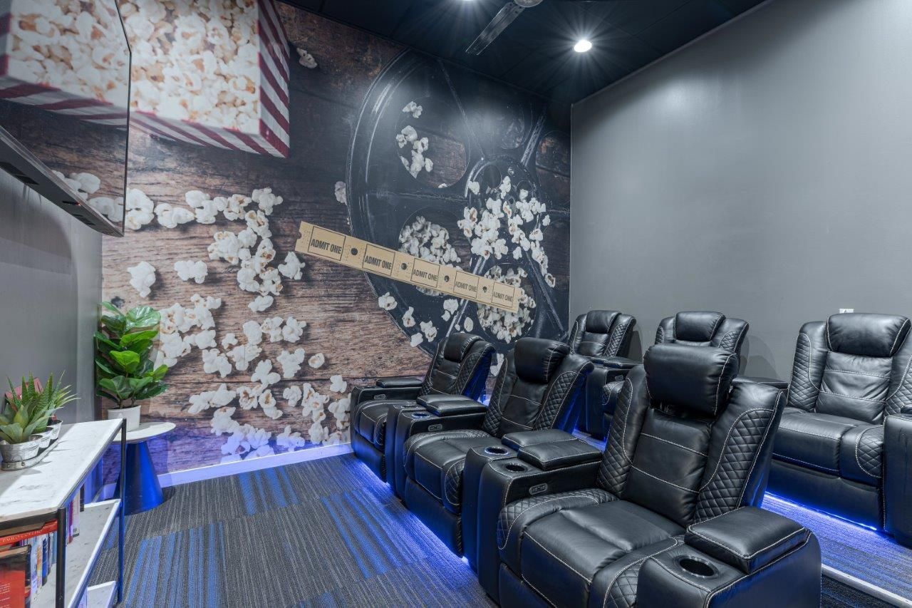 theater with black leather recliners, blue LED lighting, and a floral mural wall