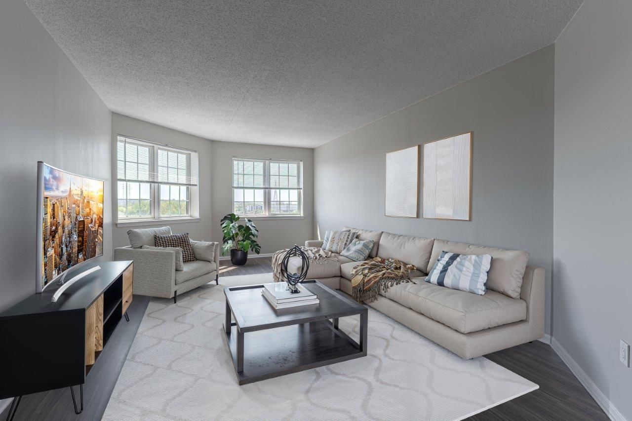 Bright modern living room with beige sectional, gray rug, coffee table, TV, and large windows