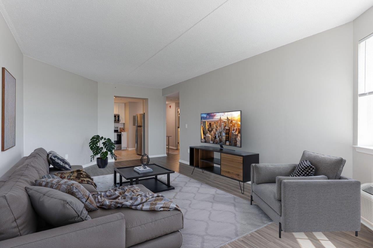 Modern living room with gray sofas, TV, coffee table, and light walls with open doorway.