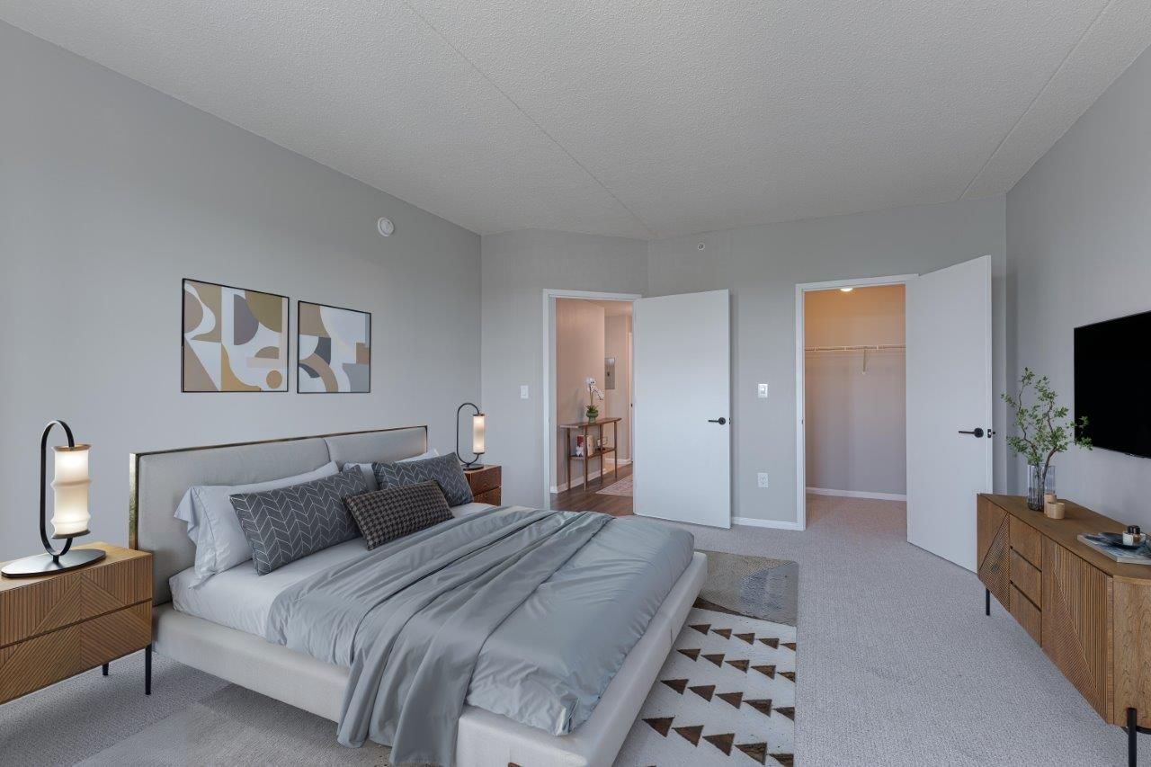 Modern bedroom with gray bedding, wood nightstands, and an open doorway to a bright hall