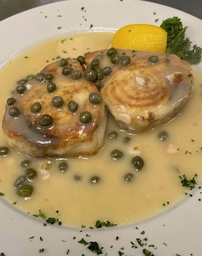 Pan-seared fish with lemon butter sauce and capers, garnished with parsley and lemon wedge on a white plate.