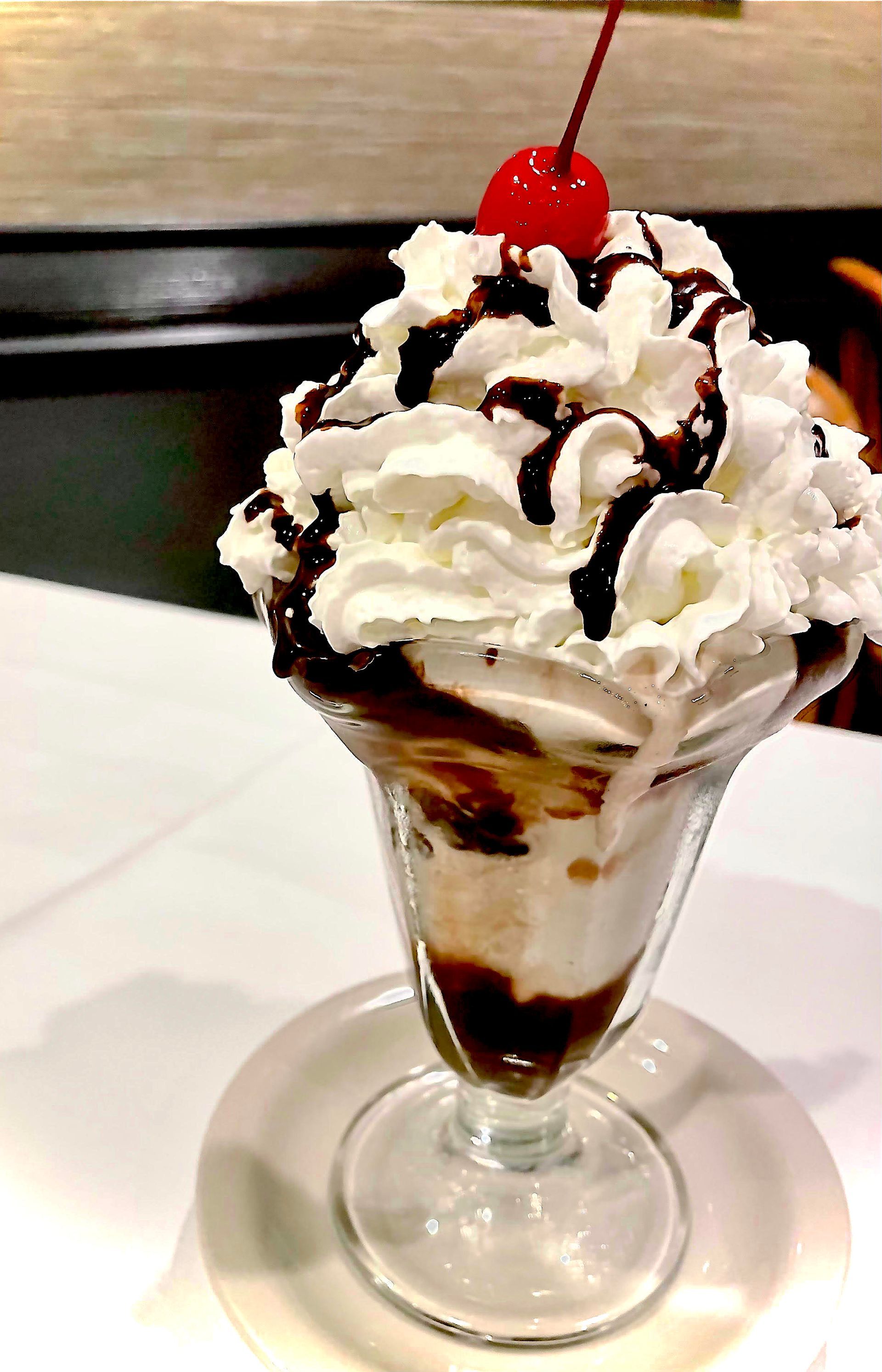 Sundae in a glass, with whipped cream, chocolate syrup, and a cherry on top.