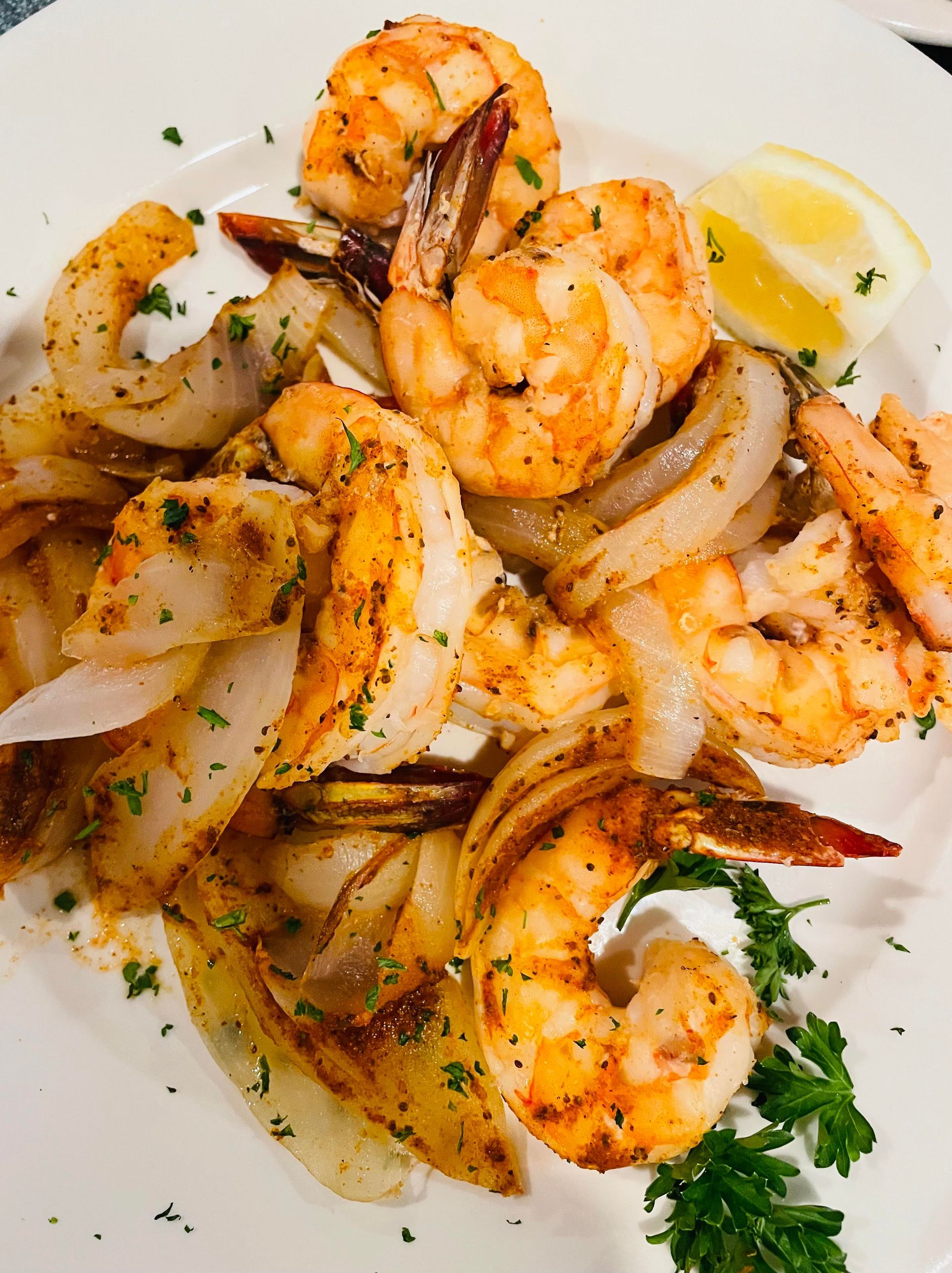 Sautéed shrimp and onions on a white plate, garnished with parsley and a lemon wedge.