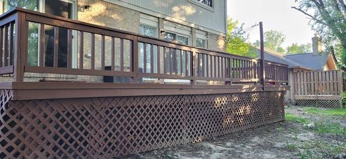 Wooden deck with brown railing and lattice siding, beside a house and backyard.