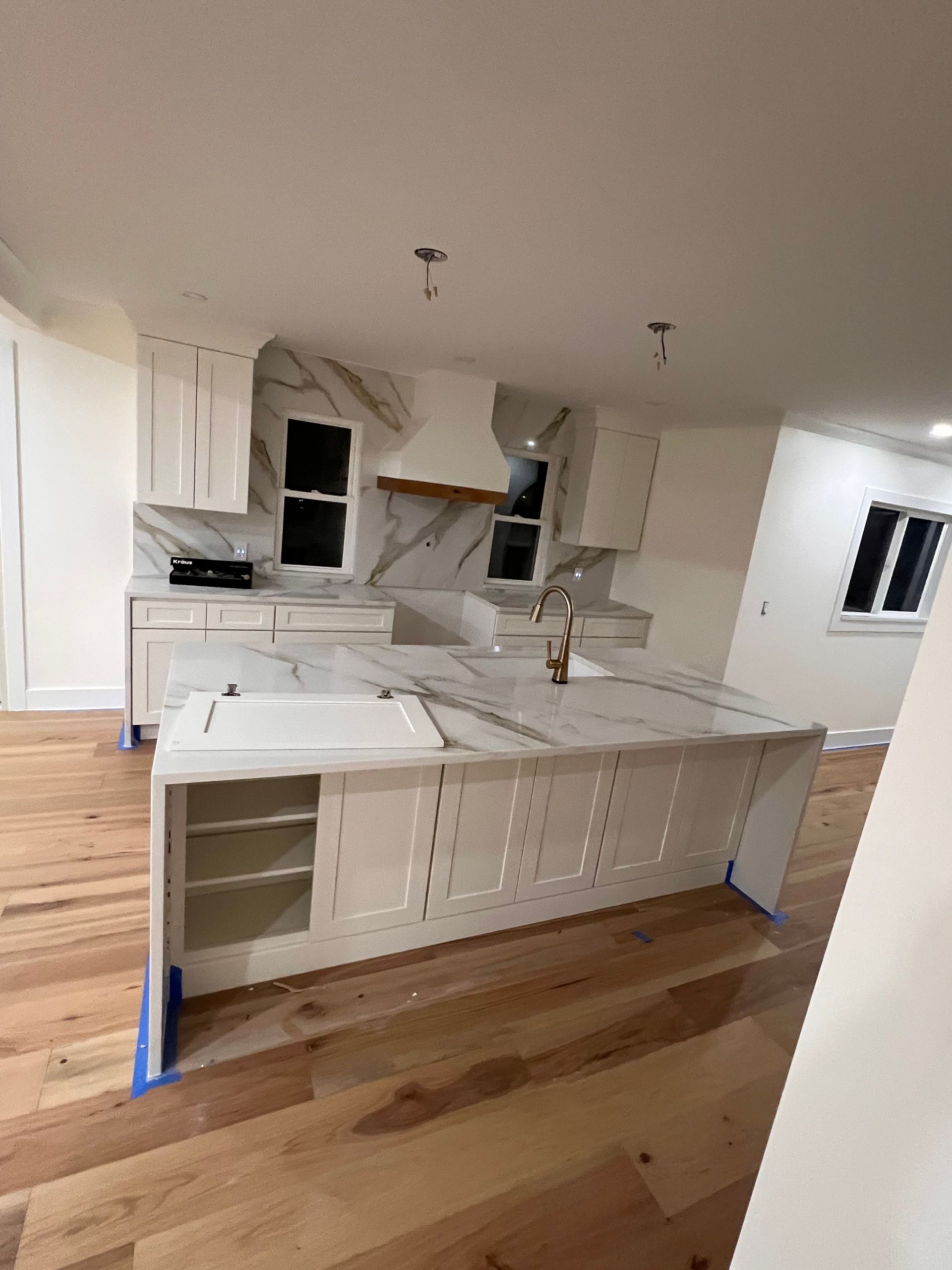 White kitchen with marble countertops and island, wood floor.