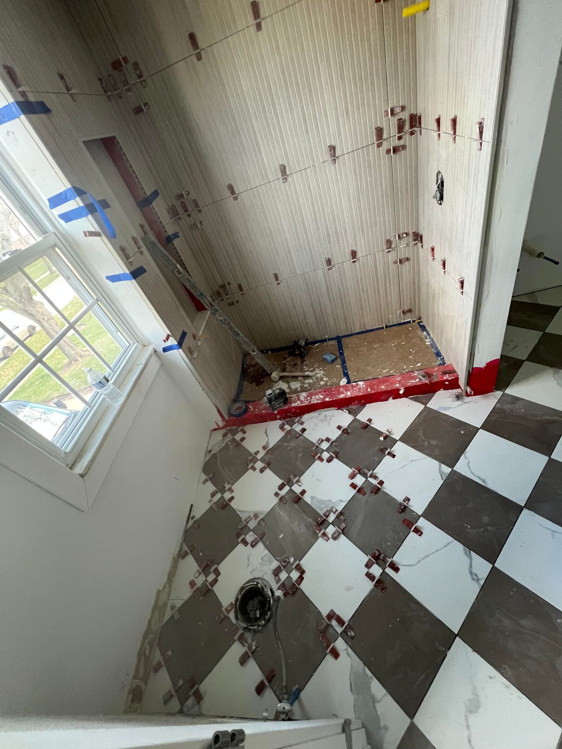 Bathroom renovation in progress; checkered floor and tiled walls with leveling spacers visible.