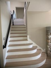Staircase with light wood treads and white risers. Black handrail on left. Beige walls.