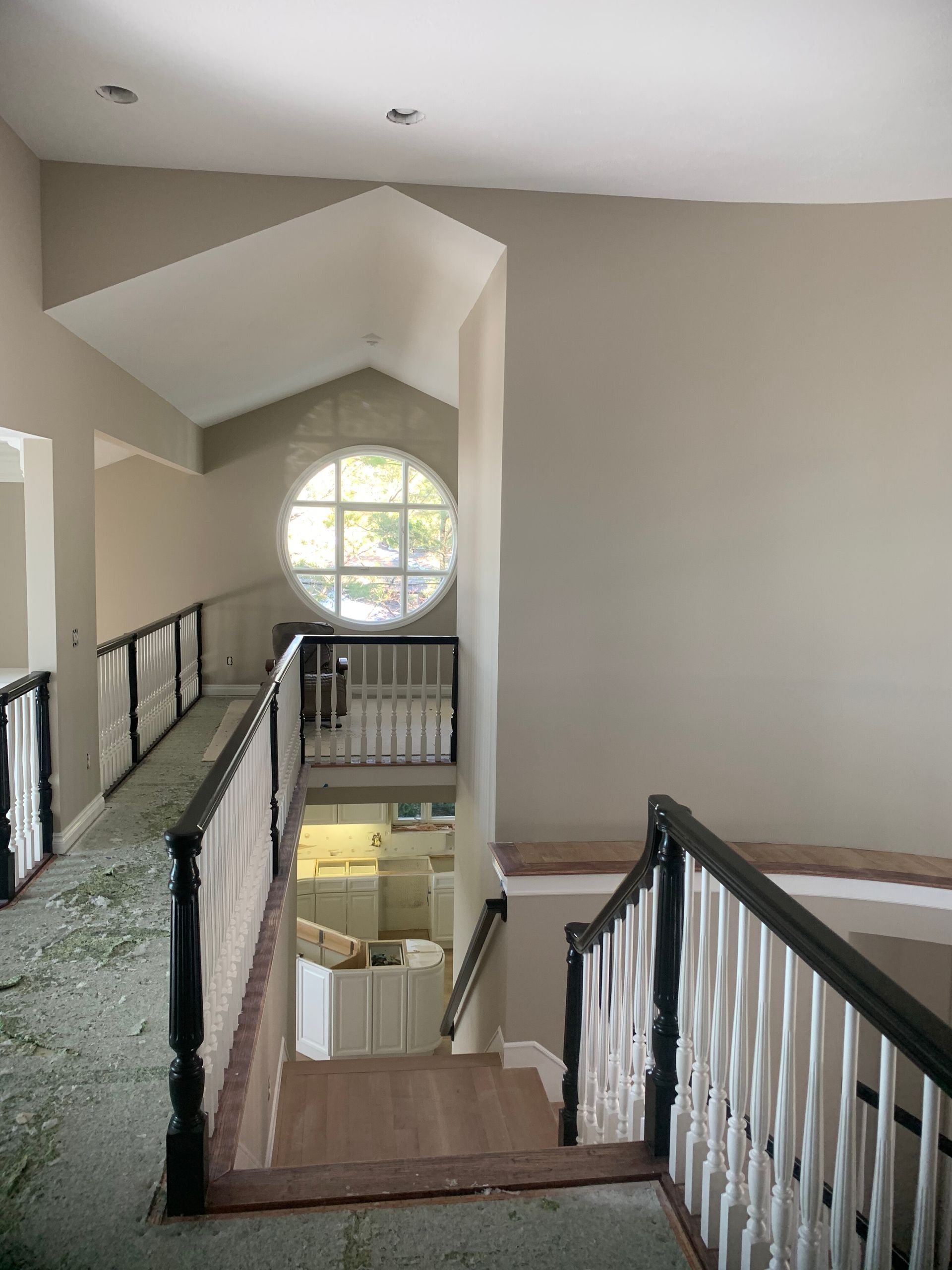 Interior view of a staircase, railing, and a landing with a round window. Neutral-colored walls and carpet.