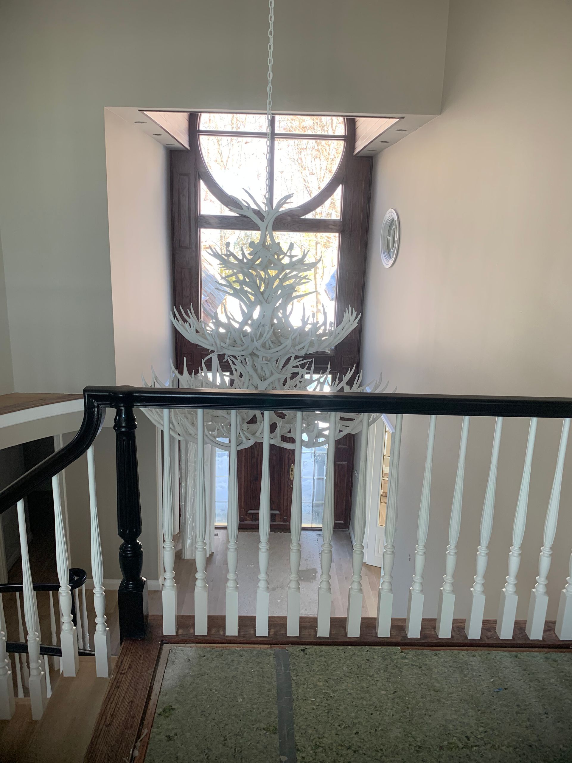 White chandelier hangs over a staircase with a black railing, leading to a tall window with natural light.