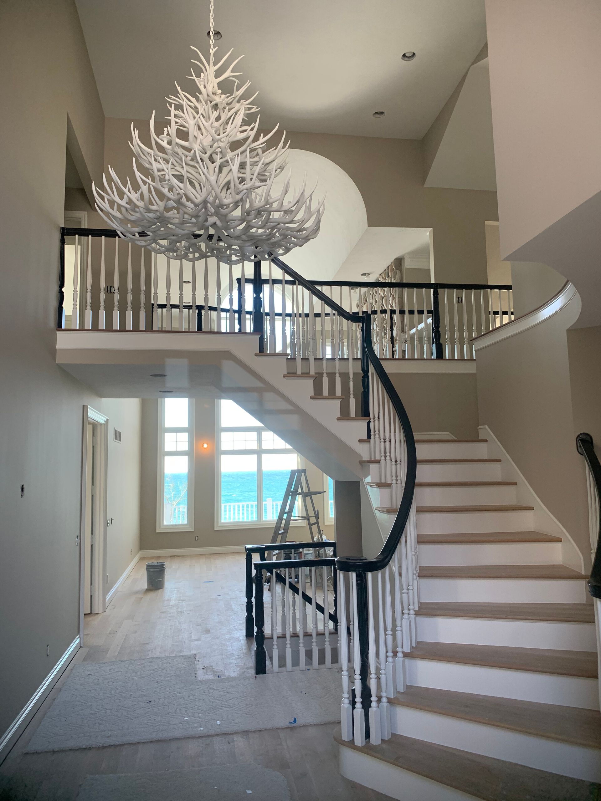 A grand staircase with white and black railings, leading to a balcony and a large chandelier.