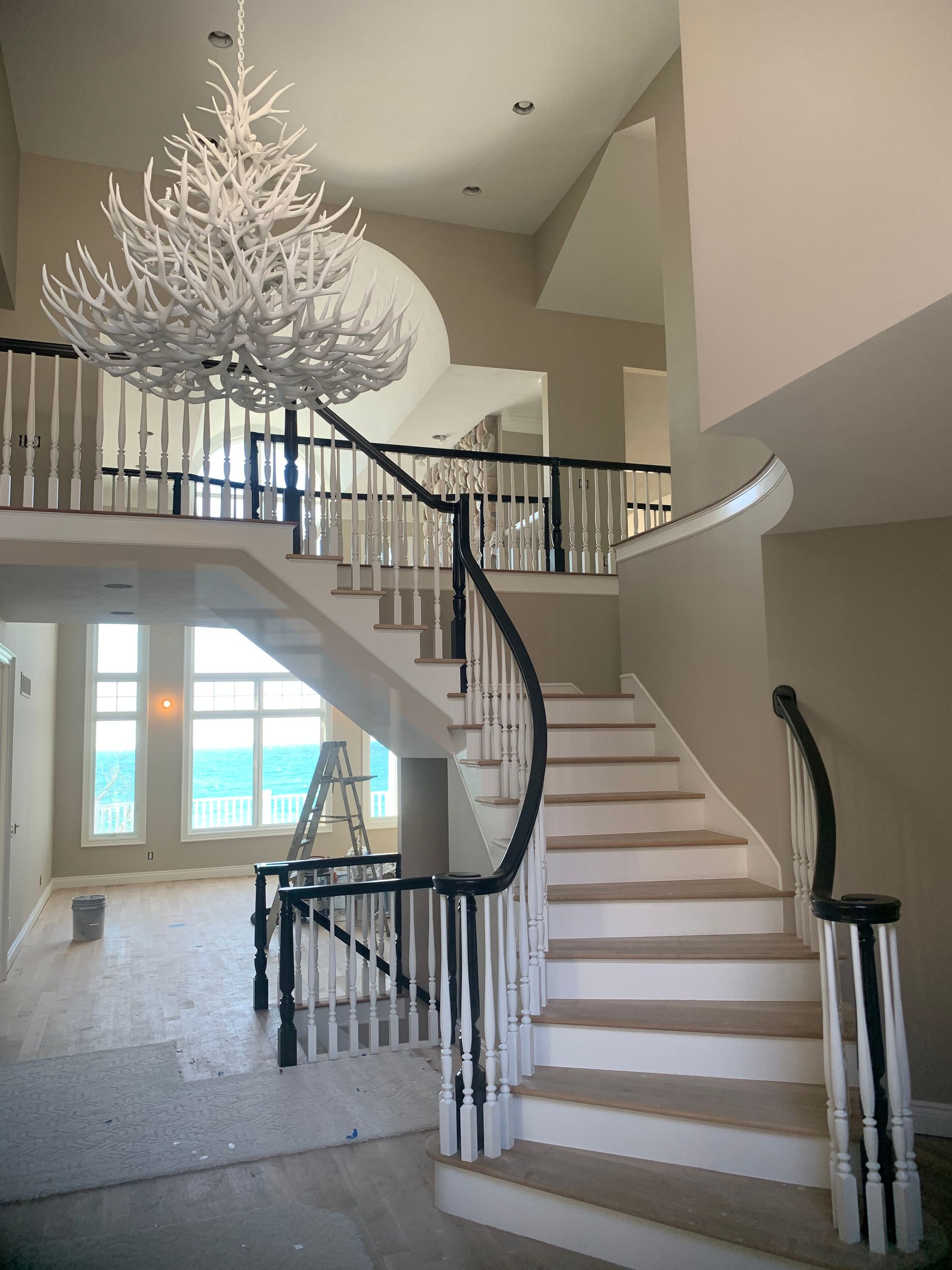 Two-story foyer with a curved staircase, chandelier, and a view of the water through large windows.
