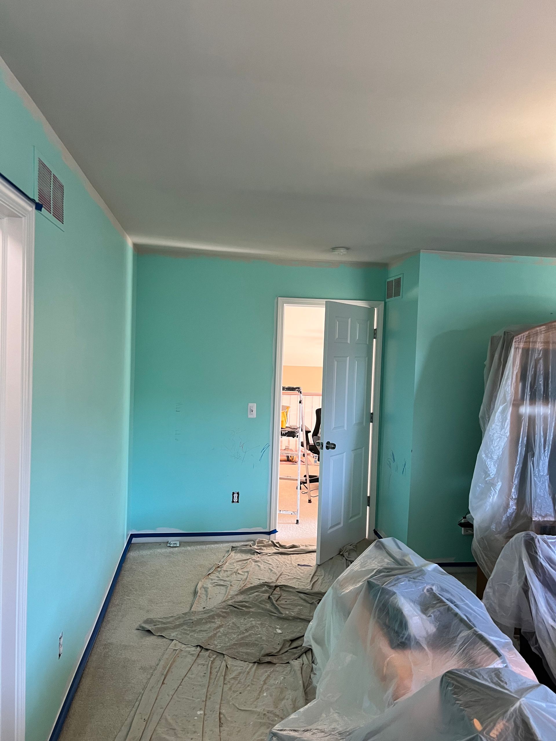 Room with freshly painted aqua walls, open doorway, and covered furniture.