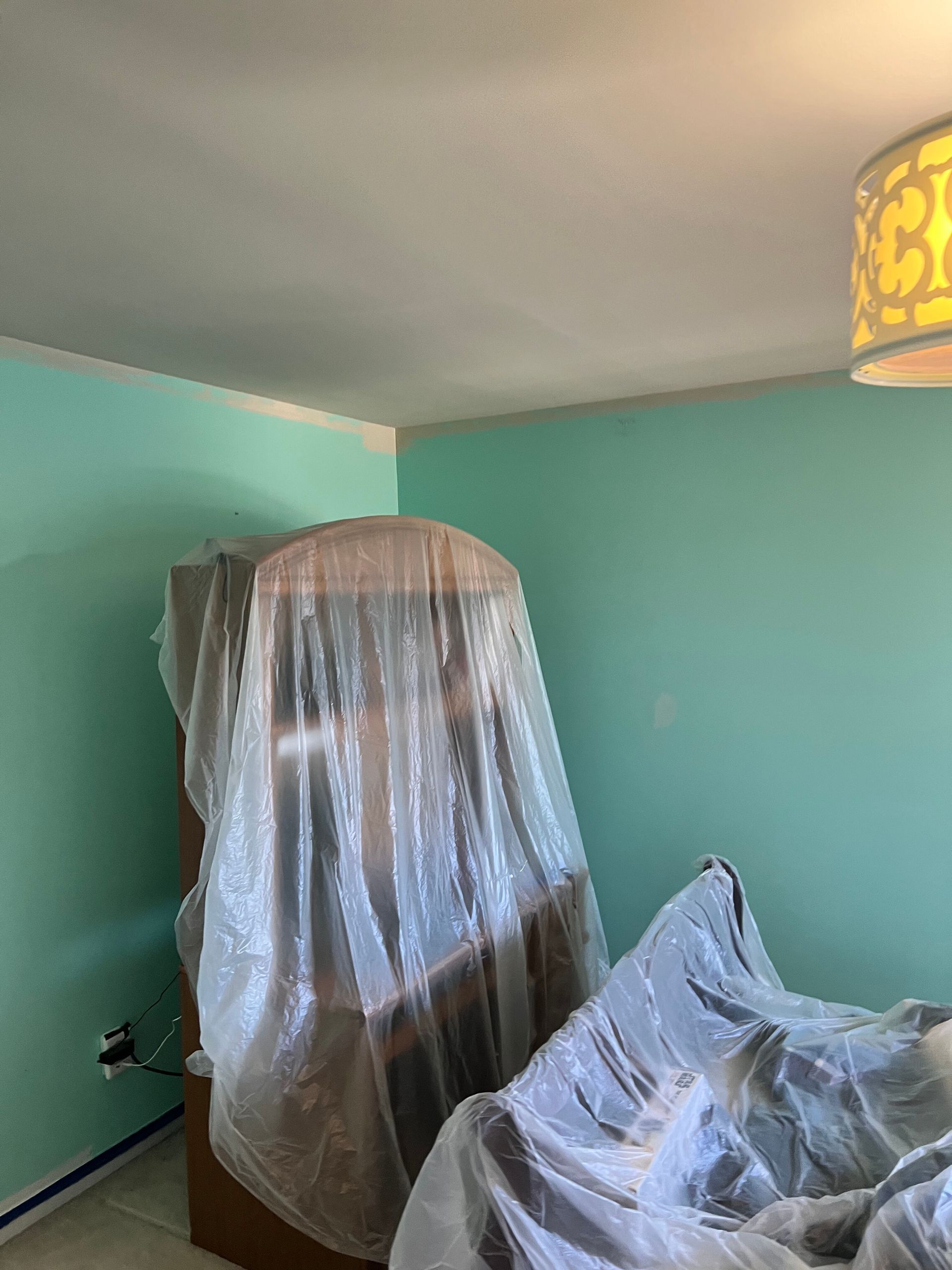 Room with turquoise walls and a covered piece of furniture. A yellow lamp hangs from the ceiling.