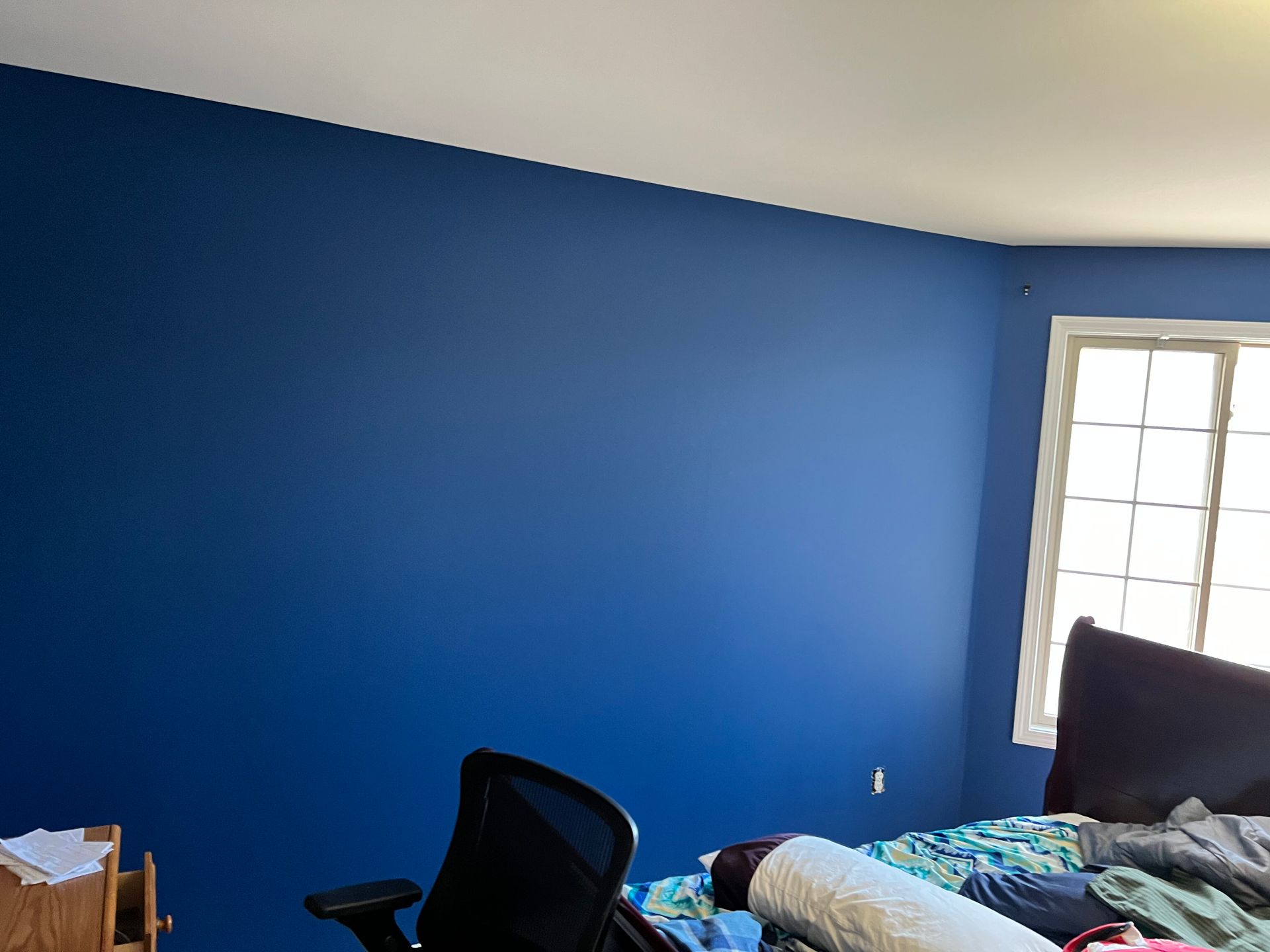 Blue wall in a bedroom with a window, bed, and office chair.