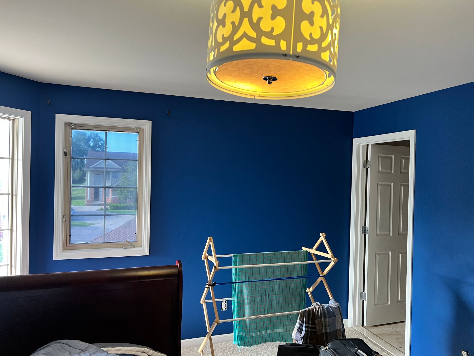 Bedroom with blue walls, a drying rack with towels, window, door, and a decorative light fixture.