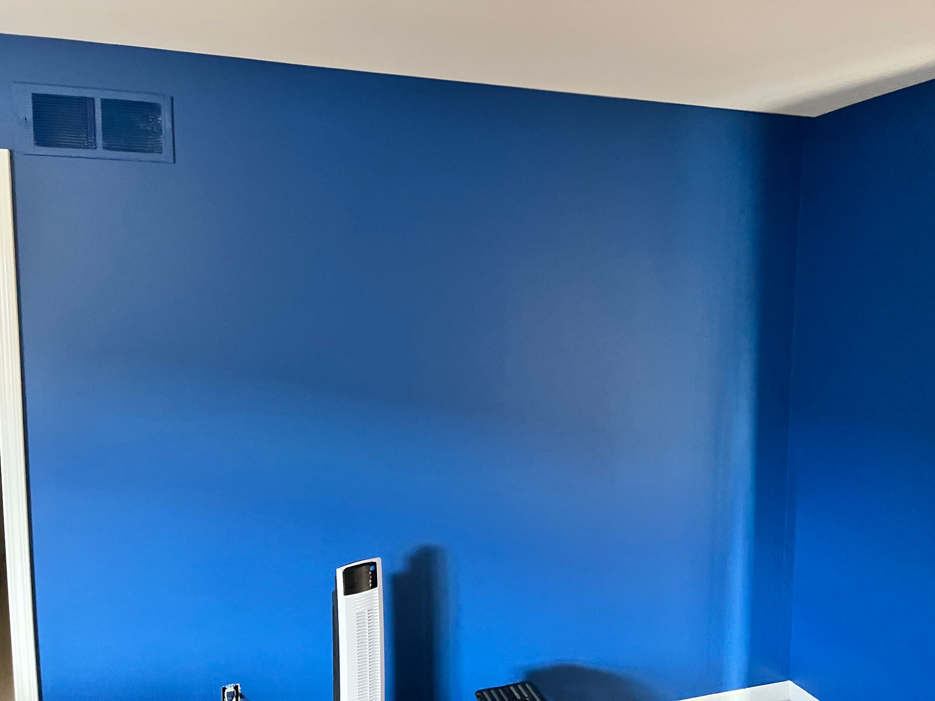 Blue painted wall with white trim and a vent. A white object is casting a shadow.