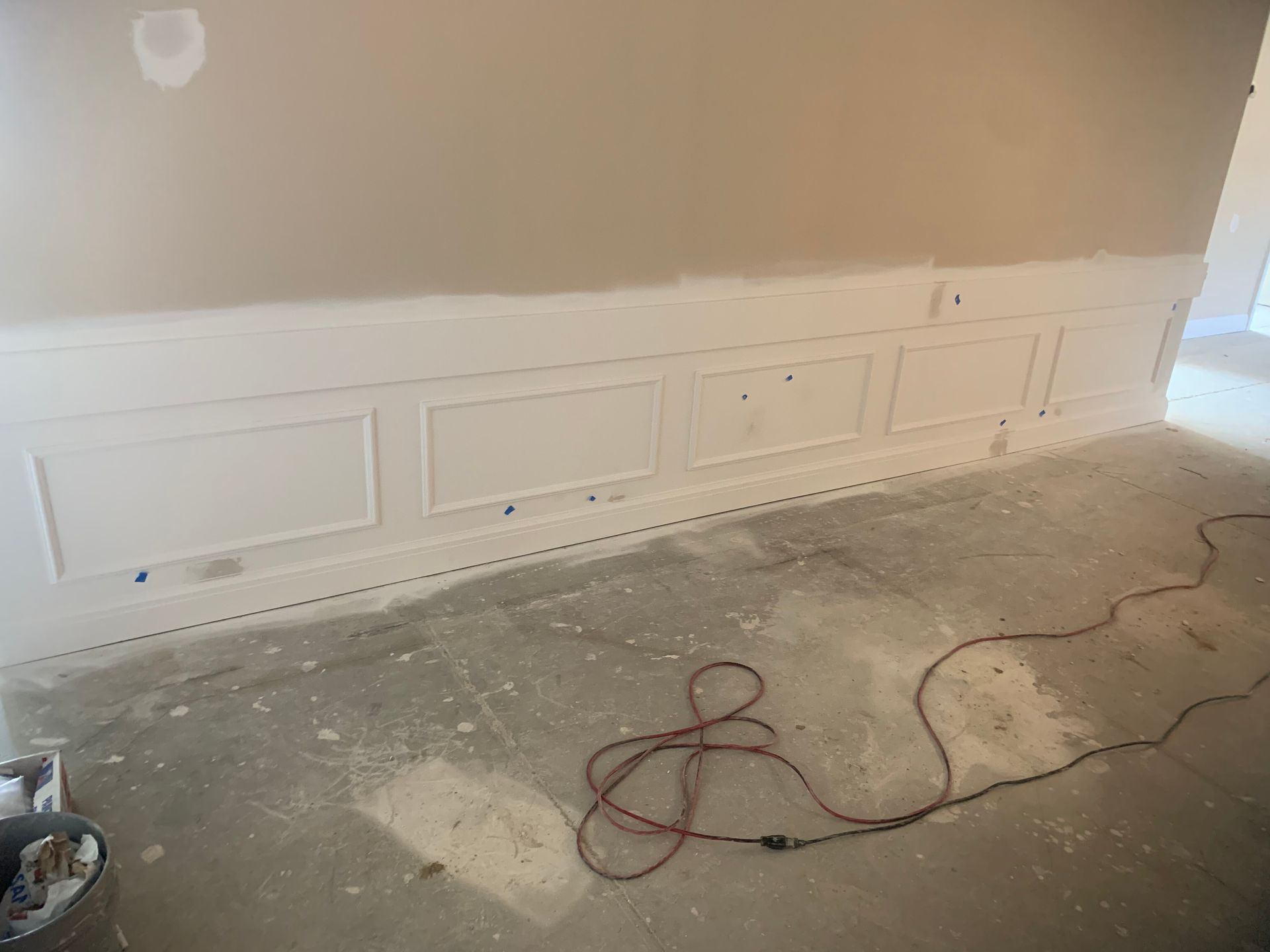 White wainscoting on a wall under construction. A power cord lies on the concrete floor.