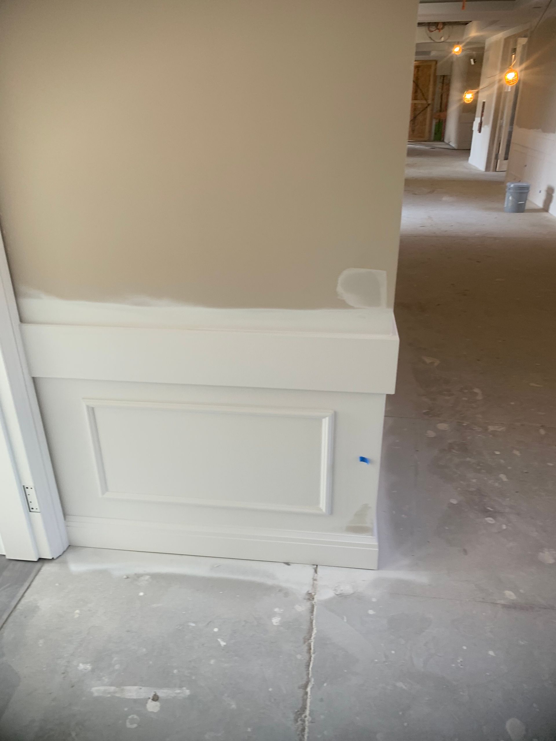 Beige wall with white wainscoting and light gray flooring in a building under construction.