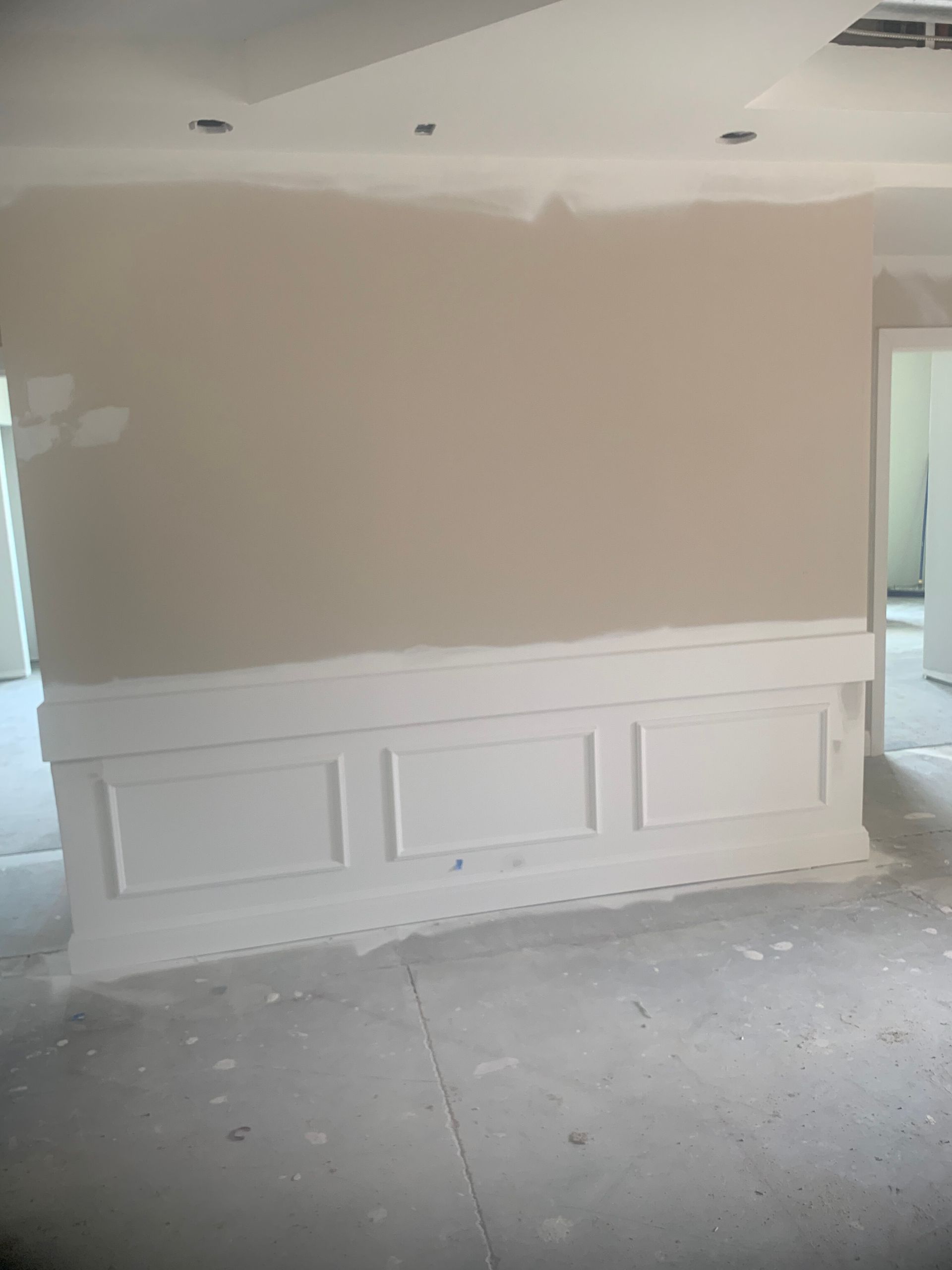 Wall with white paneling below and light beige wall above, in a room under construction.