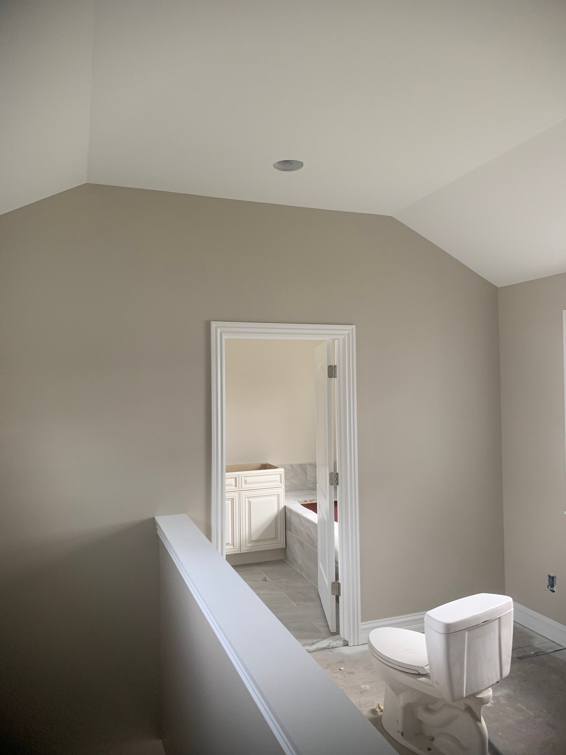 Interior view of a bathroom under construction with a toilet, open doorway, and neutral-colored walls.